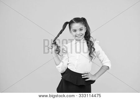 Her Twisted Hairdo. Small Girl Winding Long Hairdoaround Her Finger On Yellow Background. Little Kid