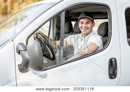 Portrait Of A Cheerful Delivery Driver In Uniform Looking Out The Window Of The White Cargo Van Vahi