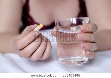 Woman Taking Pill Holding A Water Glass, Sexy Girl In Lingerie Lying On The Bed With Capsule. Concep