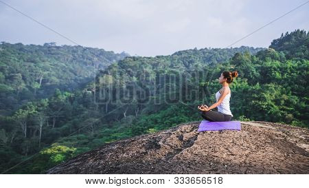 Asian Women Relax In The Holiday. Play If Yoga. On The Moutain Rock Cliff. Nature Of Mountain Forest