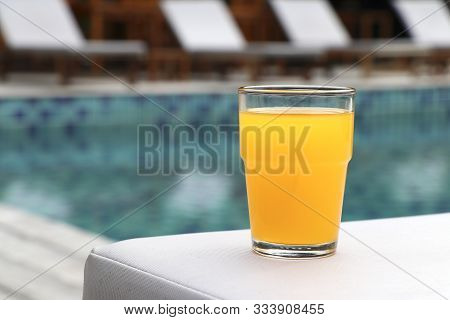 Glass Of Orange Juice Placed On A Wooden Floor By The Pool.