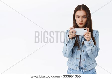Serious-looking Cute And Feminine Caucasian Woman In Denim, Holding Smartphone Horizontally, Pouting