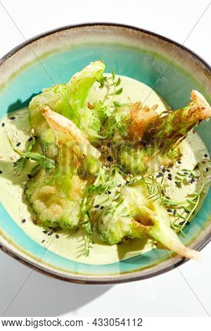 Fried tempura broccoli with peanut sauce in bowl. Vegeterian hot dish - florets cabbages roasted  in klar on white background. Veggie menu for asian restaurant. Hot vegan appetizers plant based