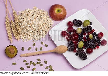 Plate With Frozen Berries. Spikelets Of Wheat And Oat Flakes On Table. Flat Lay. Pink Background