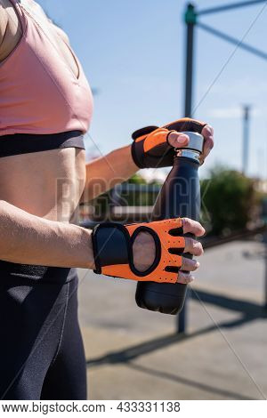 Close Up Of Woman Hands In Sport Gloves Holding Water Bottle On Sports Ground