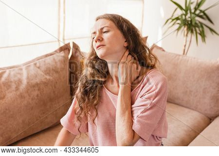 Tired young woman touch stiff neck feeling hurt joint back pain rubbing massaging tensed muscles suffer from fibromyalgia ache after long computer work study in incorrect posture sit on sofa at home