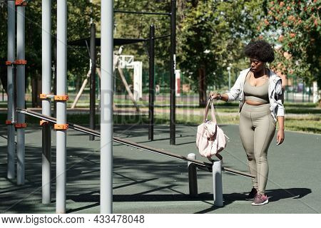 Young plus size female in sportswear putting handbag on facilities before outdoor training