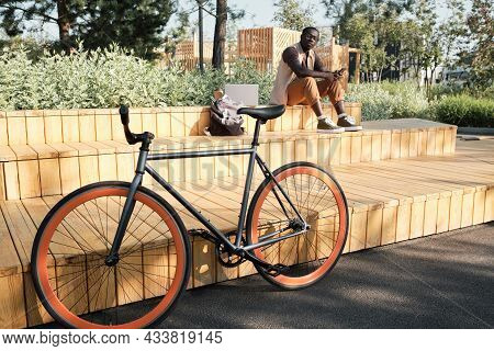 Horizontal Selective Focus Shot Of Young African American Man Sitting On Bench In Modern City Park L