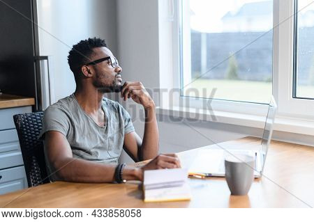 An Intelligent African-american Young Man In Glasses And Casual Shirt Sits At The Kitchen Desk With 