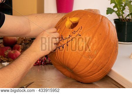 Man Is Carving Orange Pumpkin On Wooden Table. Creative Person Setting Mood For Trick-or-trickers. H