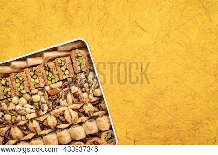 assortment of traditional Turkish baklava pastry in a tin box against handmade paper with a copy space, a dessert is well also known as persian or lebanese baklava