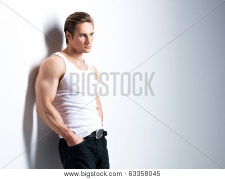 Fashion portrait of handsome young man in white shirt looking sideways poses over wall with contrast shadows.