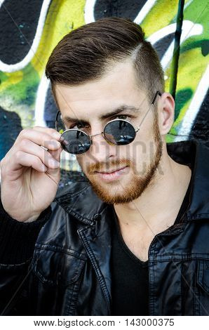 Close up portrait of cool trendy stylish sexy handsome hipster guy wearing sunglasses on the graffiti background in the city