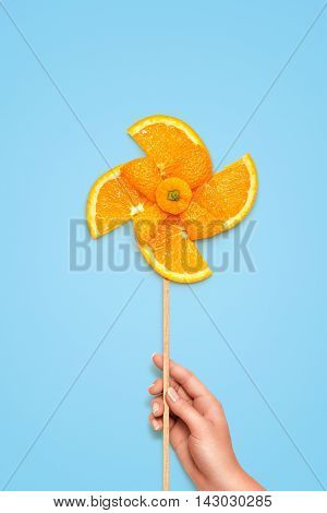 Creative still life of a yellow toy windmill made of fresh orange slices on blue background.