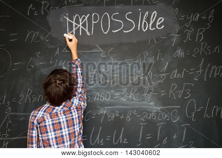 boy putting a cross over impossible on blackboard