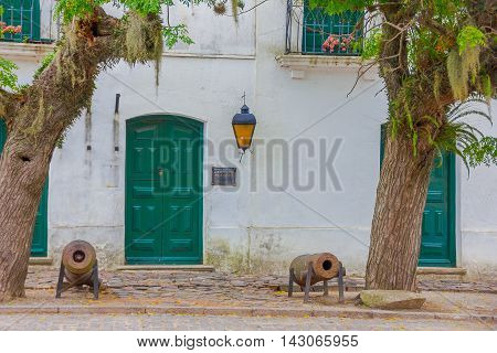 COLONIA DEL SACRAMENTO, URUGUAY - MAY 04, 2016: nice ancient ehite house with green doors and windows, two big trees in the sidewalk.