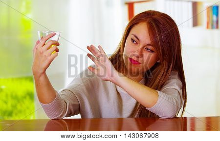 Woman wearing white sweater sitting by bar counter lying over desk next to glass and bottle, drunk depressed facial expression, alcoholic concept.
