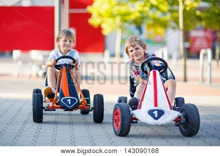 Two active little kid boys driving pedal race cars in summer outdoors. Children, best friends racing with fast speed and having fun. Twins making competition