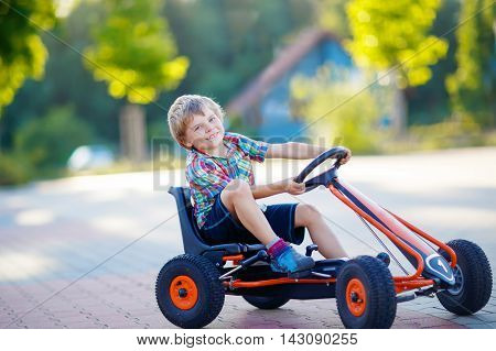 Active little kid boy driving pedal race car in summer garden, outdoors. child racing with fast speed and having fun.