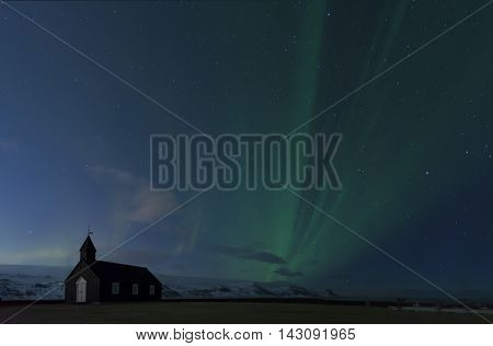 Dramatic Northern Lights Aurora Borealis dancing over the Black Church of Budir in Iceland transition concept of twilight and night
