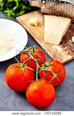 Branch of fresh red tomatoes with water drops on and parmesan or parmigiano reggiano cheese on back with grater and grated cheese on white plate and mint beam. Concept of italian cuisine ingredients