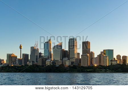 Sydney CBD skyscrapers with Sydney Tower and Royal Botanic Garden view on sunset with sun reflecting from windows. Modern urban cityscape with office buildings
