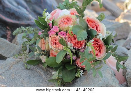 Bridal bouquet lying on the stones. Wedding bouquet of peach roses by David Austin single-head pink rose aqua eucalyptus ruscus gypsophila