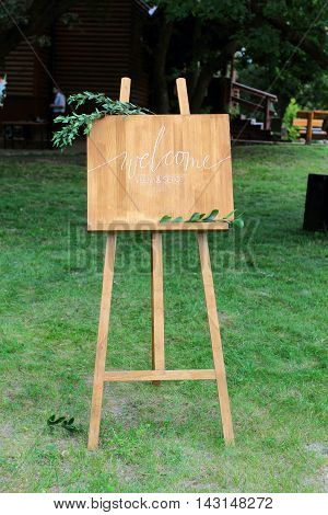 Wooden easel with a board. On the board written white paint - Welcome