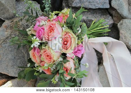 Bridal bouquet lying on the rocks. Wedding bouquet of peach roses, single-head pink rose aqua, eucalyptus ruscus, gypsophila