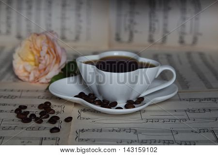 CUP OF COFFEE ON MUSICAL SHEETS AND THE ROSE