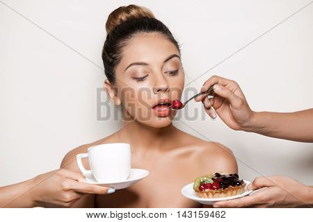 Hands offering cake and drinks to young beautiful naked girl in towel over light background.
