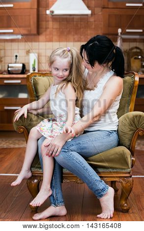 Mother and her little daughter sitting in a chair at home