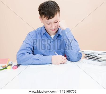 The Boy Is Writing In A Notebook At The Table