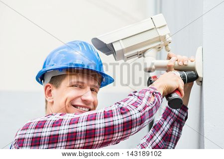Close-up Of Happy Male Technician Installing Camera On Wall