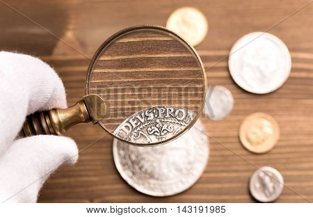 Examining old silver coin through magnifying glass on wooden table