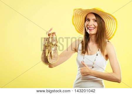 Holidays summer fashion concept. Woman in big yellow hat holding golden sandals in hand bright background.