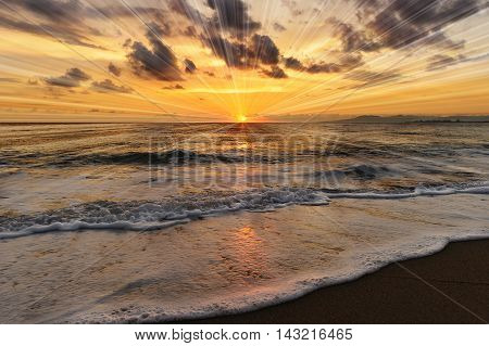 Ocean sunset rays is a brightly lit golden orange seascape with a burst of sun beams as a gentle wave rolling to the shore.