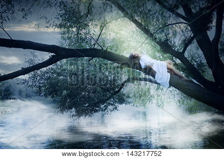 Beautiful woman in white dress lying on a tree over the river