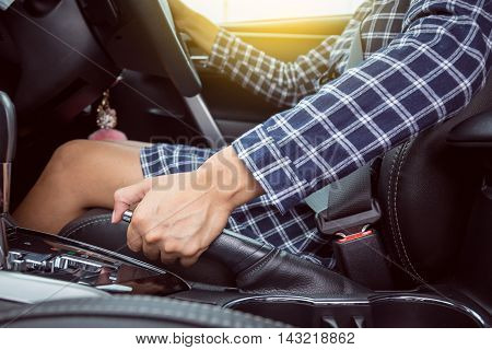 Closeup of young woman pulling handbrake lever in car