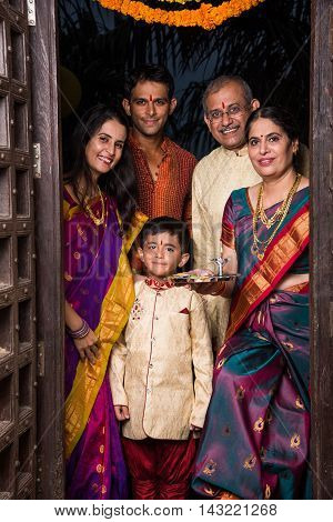 indian family group photo while entering house with puja thali at old antique door, gruha pravesh
