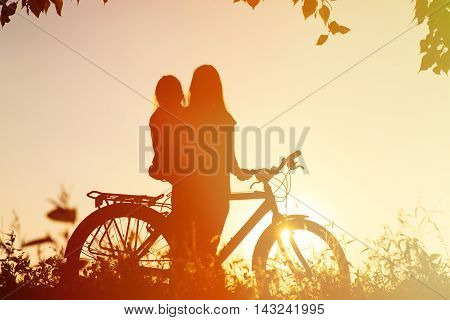 silhouette of mother and little daughter riding bike at sunset