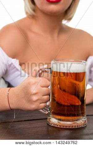 Beautiful young blond girl in dirndl drinks out of oktoberfest beer stein. Isolated on white background. sits by the table. close-up mug