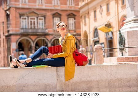 Young female student dressed casually sitting with book on the central square near university of Bologna in Bologna city in Italy.