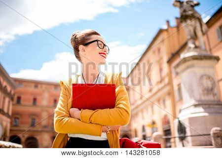 Young female student dressed casually sitting with book on the central square near university of Bologna in Bologna city in Italy.