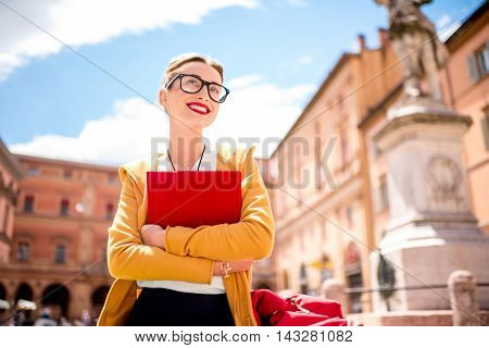 Young female student dressed casually sitting with book on the central square near university of Bologna in Bologna city in Italy.