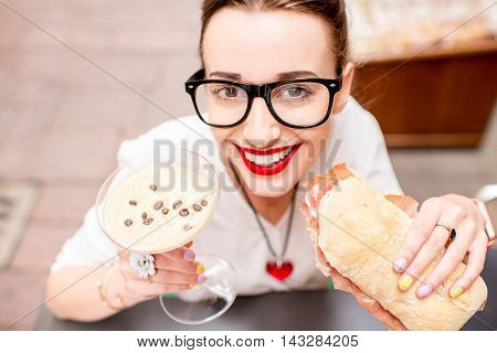 Young woman with shakerato coffee drink and panini with prosciutto outdoor.