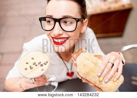 Young woman with shakerato coffee drink and panini with prosciutto outdoor.
