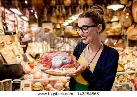 Young woman sitting near the food shop with traditional italian appetizer on the blurred food showcase background in Bologna city. Bologna is the gastronomic center of Italy