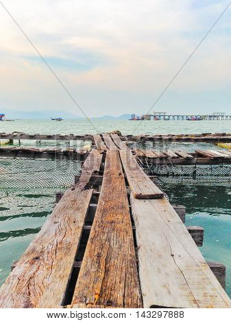 A wooden fishing bridge floating on the sea in Phuket , Thailand, with partly cloud sky and pier as a background.