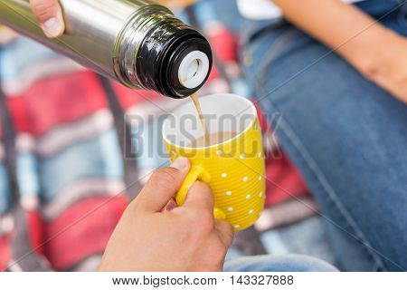 Young couple on a picnic in a park. Close up of a man pouring hot coffee from a thermos bottle